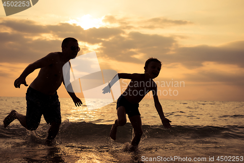 Image of Father and son playing on the beach at the sunset time.