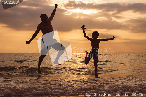 Image of Father and son playing on the beach at the sunset time.