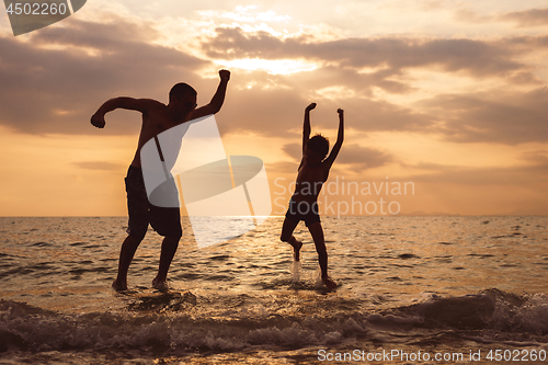 Image of Father and son playing on the beach at the sunset time.