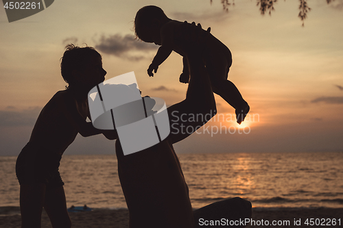 Image of Father and two sons  playing on the beach at the sunset time.