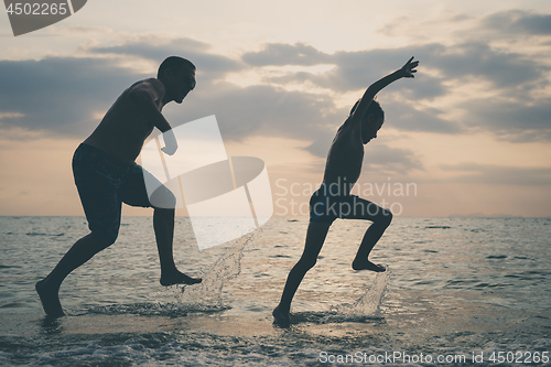 Image of Father and son playing on the beach at the sunset time.