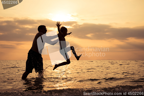 Image of Father and son playing on the beach at the sunset time.