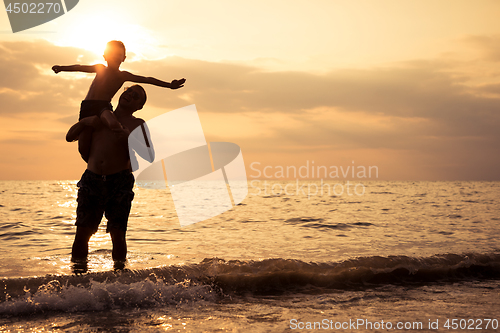 Image of Father and son playing on the beach at the sunset time.