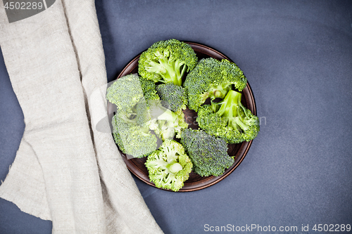 Image of Fresh green organic broccoli in brown plate and linen napkin.