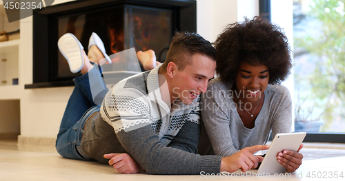Image of multiethnic couple using tablet computer on the floor
