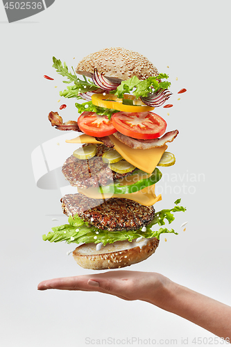 Image of Deliciouse homemade burger on a woman hand with flying fresh ingredients on a white background. Copy space.