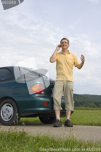 Image of Man with mobile phone beside his car