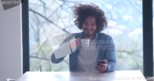 Image of young man drinking coffee and using a mobile phone  at home