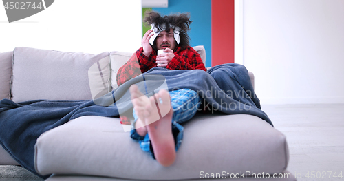 Image of sick man is holding a cup while sitting on couch