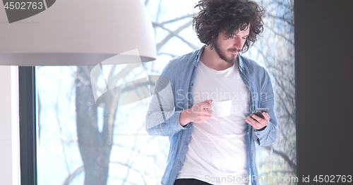 Image of young man drinking coffee and using a mobile phone  at home