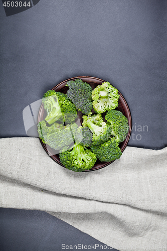 Image of Fresh green organic broccoli in brown plate and linen napkin.