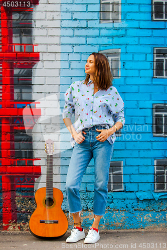 Image of smiling woman in jeans and a blue shirt stands against the wall 