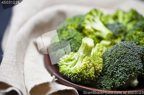 Image of Fresh green organic broccoli in brown plate and linen napkin.