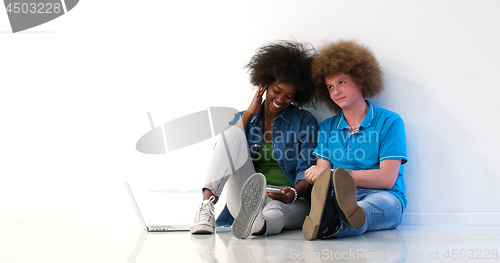 Image of multiethnic couple sitting on the floor using a laptop and table