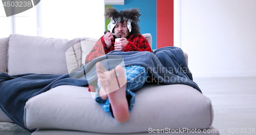 Image of sick man is holding a cup while sitting on couch