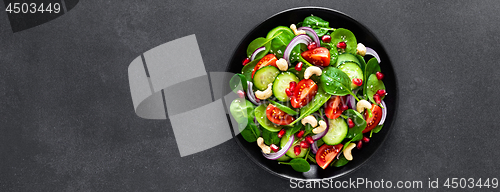 Image of Spinach salad with fresh cucumbers, tomato, onion, pomegranate, sesame seeds and cashew nuts on black background. Healthy vegan food. Top view. Banner