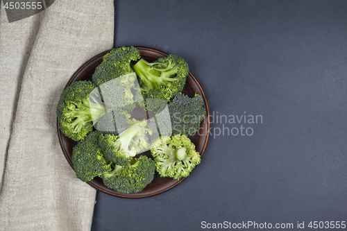 Image of Fresh green organic broccoli in brown plate and linen napkin.