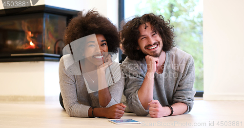 Image of multiethnic couple lying on the floor  in front of fireplace