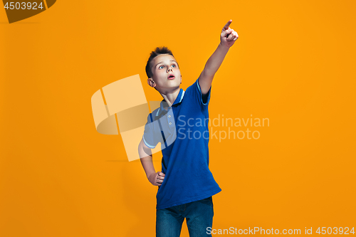 Image of The happy teen boy pointing to you, half length closeup portrait on orange background.