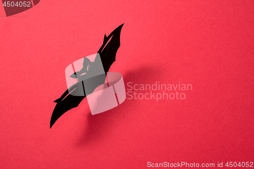 Image of Handcraft paper bat on a red background with shadow and copy space for text. Layout to Halloween. Flat lay