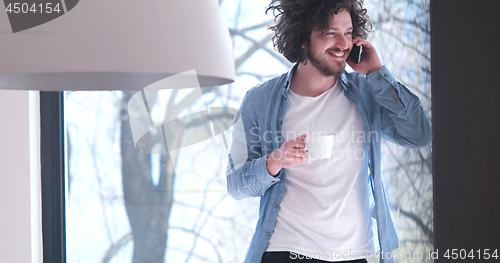 Image of young man drinking coffee and using a mobile phone  at home