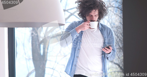 Image of young man drinking coffee and using a mobile phone  at home