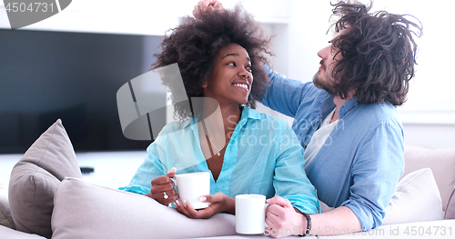 Image of multiethnic couple sitting on sofa at home drinking coffe