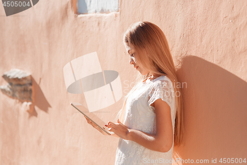 Image of beautiful young woman in white dress using tablet