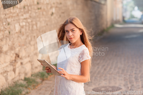 Image of beautiful young woman in white dress using tablet