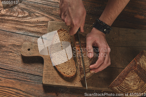 Image of fresh bread cut man\'s hands on wooden board