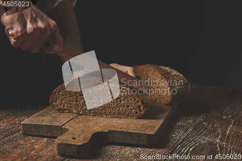 Image of men\'s hands cut homemade a dark bread