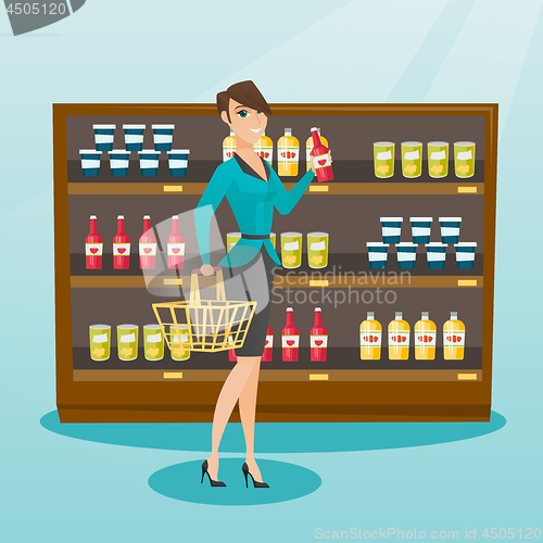 Image of Woman holding shopping basket and bottle of sauce.