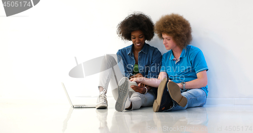 Image of multiethnic couple sitting on the floor using a laptop and table