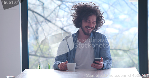 Image of young man drinking coffee and using a mobile phone  at home