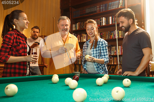 Image of Young men and women playing billiards at office after work.