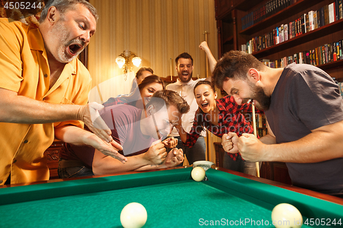 Image of Young men and women playing billiards at office after work.