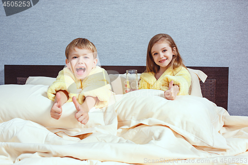 Image of Happy laughing kids, boy and girl in soft bathrobe after bath play on white bed