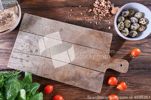 Image of Wooden board on the kitchen table around boiled quail eggs in a bowl, pieces of nuts, tomatoes, meat and greens. Copy space. Ingredients for Healthy Salad. Flat lay