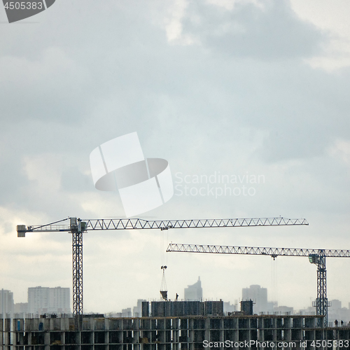 Image of Construction cranes against the background cityscape and cloudy sky. Aerial photo from the drone.