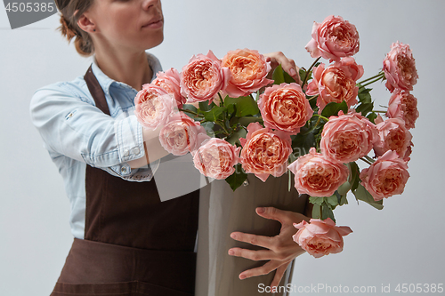 Image of Girl florist with a big bouquet of pink roses around a gray background. The concept of a flower shop