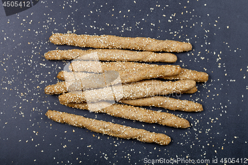 Image of Italian grissini or salted bread sticks with sesame seeds on bla