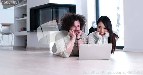 Image of young multiethnic couple using a laptop on the floor