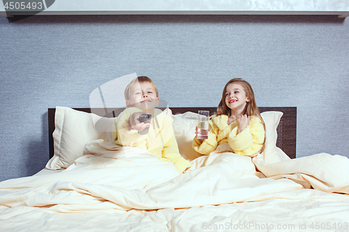 Image of Happy laughing kids, boy and girl in soft bathrobe after bath play on white bed