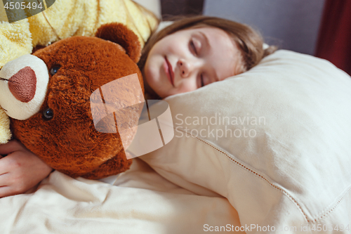 Image of child little girl sleeps in the bed with a toy teddy bear