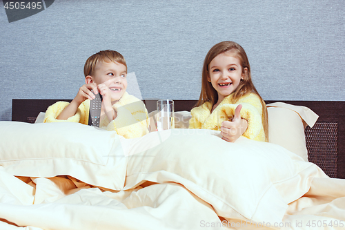 Image of Happy laughing kids, boy and girl in soft bathrobe after bath play on white bed