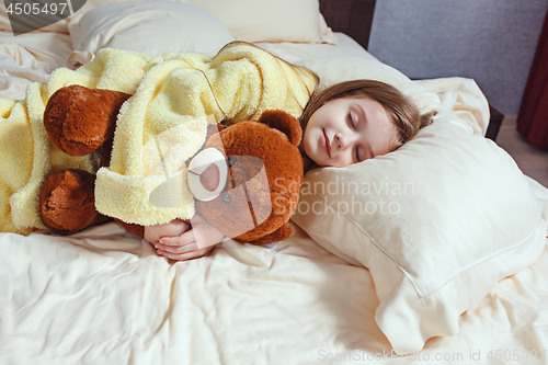 Image of child little girl sleeps in the bed with a toy teddy bear