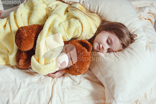 Image of child little girl sleeps in the bed with a toy teddy bear