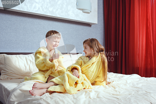 Image of Happy laughing kids, boy and girl in soft bathrobe after bath play on white bed