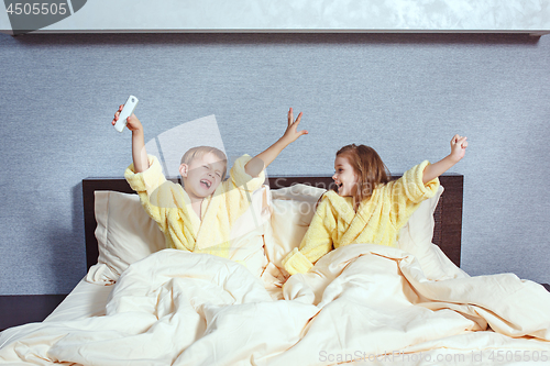 Image of Happy laughing kids, boy and girl in soft bathrobe after bath play on white bed