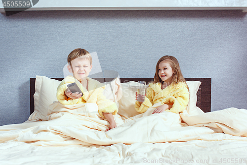 Image of Happy laughing kids, boy and girl in soft bathrobe after bath play on white bed